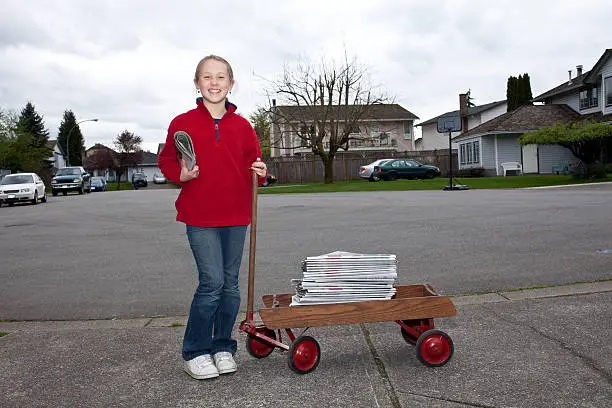 Photo of Young girl delivering newspapers with wagon in suburban neighborhood.