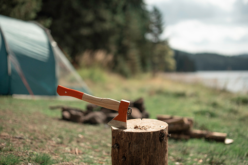 Outdoor nature lifestyle. Axe in wooden beam near tent for splitting wood.