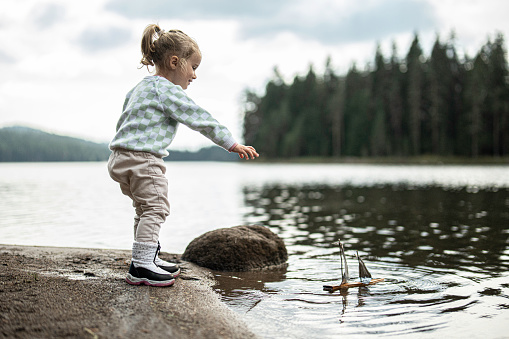 Happy little cute girl jumping from rock in water of mountain lake to her mother.