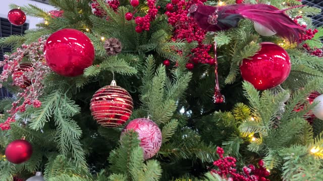 New Year's Christmas tree stands with red toys and an artificial bird of raspberry color, clusters of rowan berries of green color, needles lights glow yellow, cones on the tree