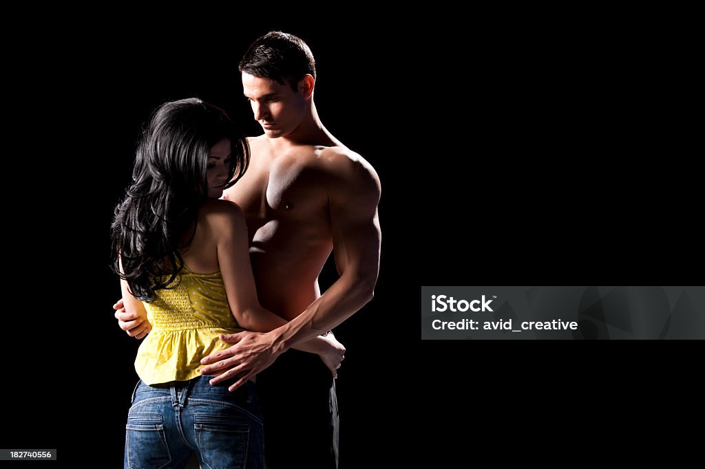Intimate Couple Resisting Tempation An intimate young couple cautiously embracing while the girl resists the temptation to give herself to her male partner. Dramatic lighting, shot against a black background. Couple - Relationship Stock Photo