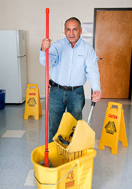 Senior Caucasian male janitor and mid-adult female janitor of African-American ethnicity together, broom and mopping the stairs at the school
