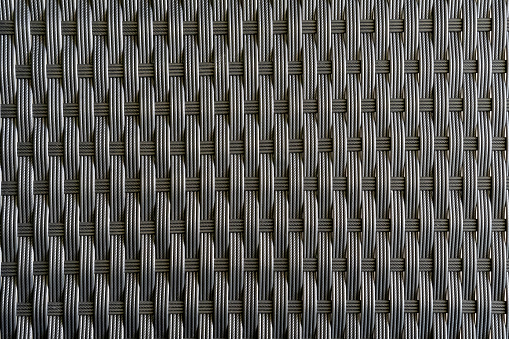 Artificial rattan background in black dark grey color, basket woven texture pattern backdrop for outdoor furniture product manufacturing and interior design decoration
