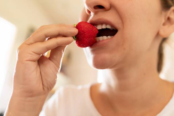 istock woman puts strawberry in mouth 1827424703