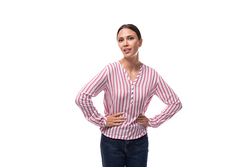 young slender well-groomed brunette leader woman with a ponytail hairstyle dressed in a striped blouse holds her hands on her waist.