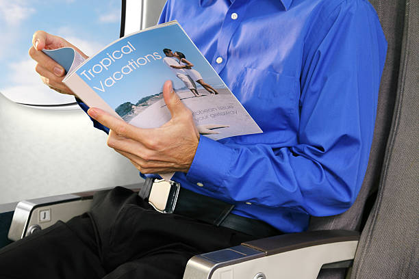 Travel Magazine XXXL.  Businessman reading a travel magazine while flying on a commerical airplane. gchutka stock pictures, royalty-free photos & images