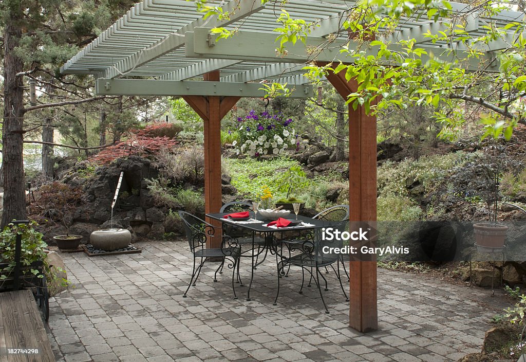 patio "Landscaped outdoor patio with pergola, brick pavers, water feature and seating. Soft lighting accentuates drying pavers after a passing storm." Pergola Stock Photo