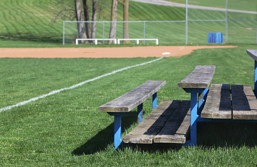 A baseball diamond with wooden benches for spectators is all set up and ready for a sunny afternoon game in early spring.