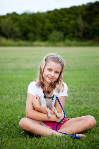 Little girl sitting on green grass holding her puppy in the outdoors. Click to see more...