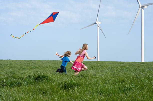 Children playing with a kite and toy glider near wind turbines.