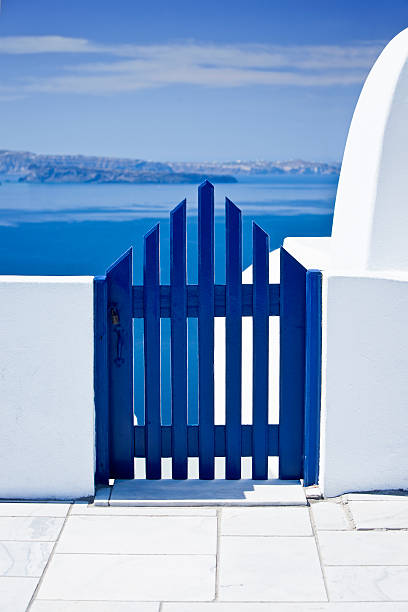 Bright morning scene of Oia Village Santorini is dominated by a blue gate with green bushes