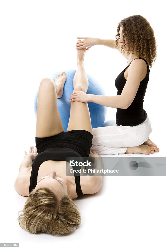 two young women doing therapeutic exercises Physical therapy. A female physiotherapist is assisting a young woman in therapeutic exercises. Exercises with fitness ball. Rehabilitation. Studio shot. High key. Isolated on white background. XXXL (Canon Eos 1Ds Mark III) Exercising Stock Photo