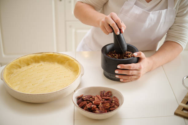 istock Woman using mortar and pestle while making pecan pie. Process of cooking pecan pie in home kitchen for American Thanksgiving Day. 1827535714