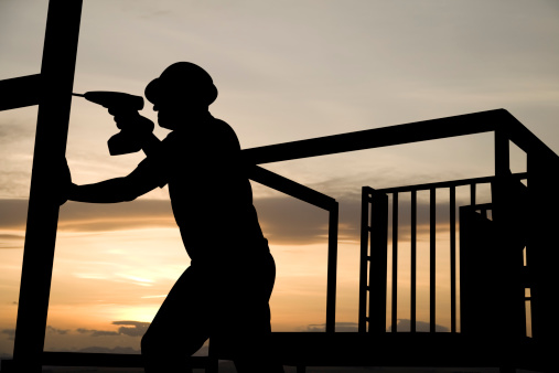 A construction worker uses a drill as he works on a building frame.