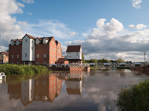 Tewkesbury Old Mill and footbridge wide shot "Old flour mill standing on the river in Tewkesbury, now converted to residential use, with footbridge leading across the river." old flour mill stock pictures, royalty-free photos & images