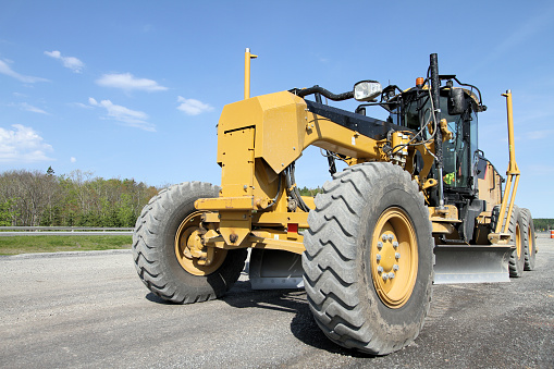 Close-up, front quarter view of a road grader on a new highway construction site.