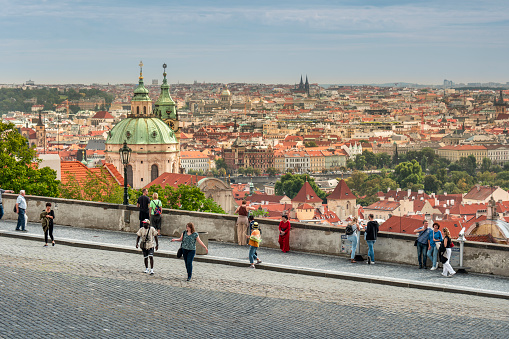 Prague, Czechia - September 13, 2022:  People look over the Prague city skyline view from the Prague Castle of the residential houses in the Mala Strana and the Towers of the Church of Saint Nicholas, Czech republic