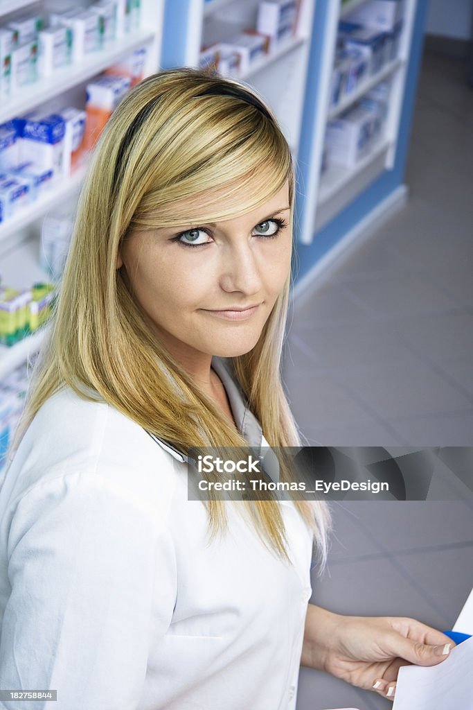 Pharmacy Technician Holding a Prescription "Pharmacy Technician standing at a checkout counter holding a prescription for medicine, boxes of medication sit on the shelf in the background. Vertical shot." 20-29 Years Stock Photo