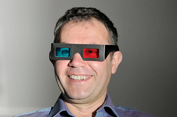 A mature man wearing 3-D glasses is amused at something he sees, almost certainly three-dimensional; could be TV, a movie or a game.