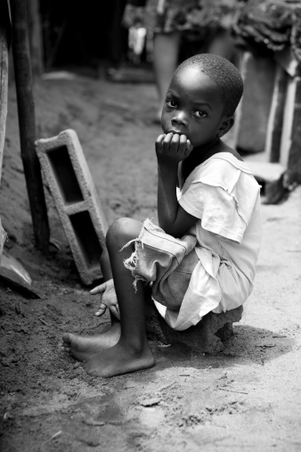 A skinny African boy sitting alone.