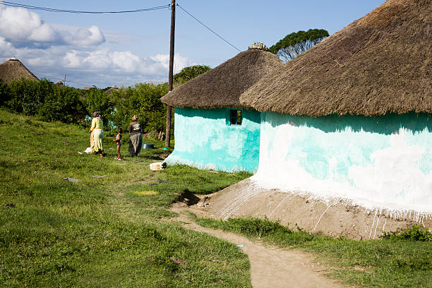 Ramabanta, Lesotho - September 20, 2017: adult african woman in traditional blanket dress in authentic village, old basotho woman near her clay round house with thatched roof, ethnic sotho people life