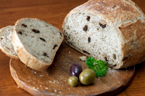 Sliced olive bread on a cutting board with olives.