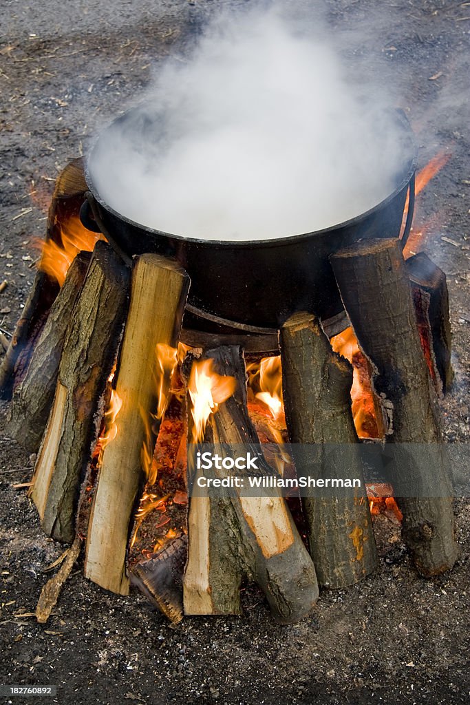 Black Cauldron on Wood Fire A large black cooking pot used to make maple syrup.  Natural logs burning around the pot heat the maple syrup to the correct temperature. Black Color Stock Photo