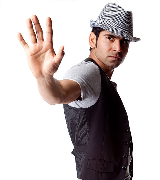 Indian male dancer wearing a hat gesturing with hand in the camera to stop on white background