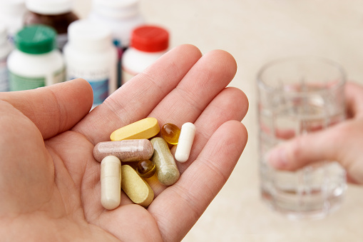 Health conscious person holding a variety of natural vitamins, supplements and herbal remedies, while their other hand holds a glass of water ready to take the pills.