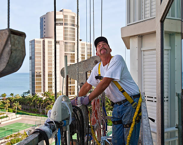 Construction Work Man is raising himself on a scaffold to do repair work on a high rise. swing staging stock pictures, royalty-free photos & images