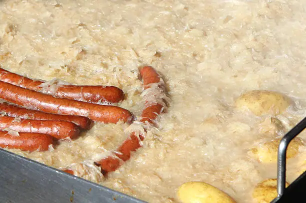 A large catering pan of potato rosti and bratwurst sausages cooking outside in Switzerland.   This image was taken at the ski resort of Kleine Scheidegg in the Bernese Oberland.