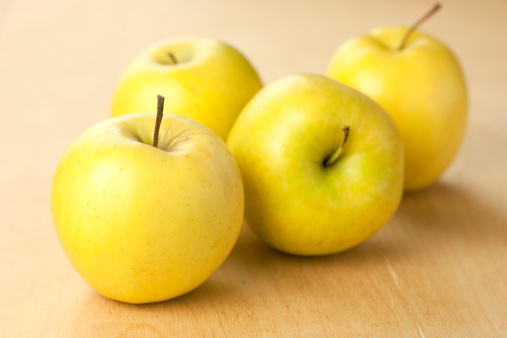 four yellow apples on wooden table