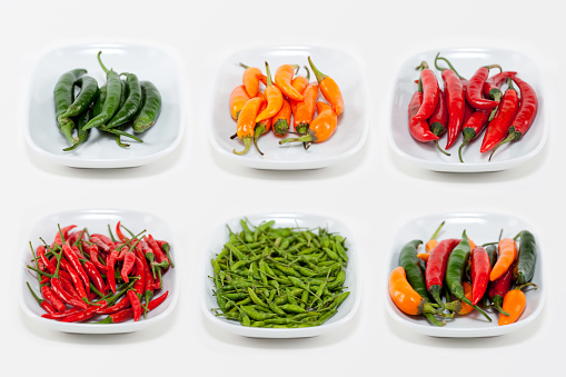 One green pepper in the foreground and four red peppers in the background. Foreground and background with black pattern. Concept for individuality or leader. Immature vs mature.