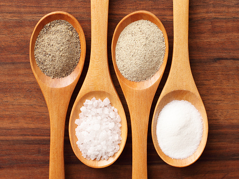 Four spoons with salt and pepper on them. From left to right: ground black pepper, rock salt, white ground pepper, table salt