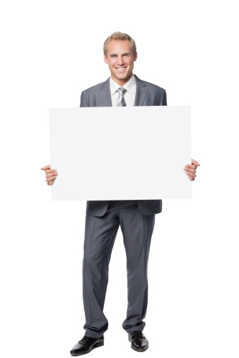Handsome businessman smiles widely while holding up a blank placard. Vertical shot. Isolated on white.