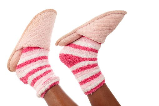 Girl's legs with cozy pink slippers and colorful socks on white background.