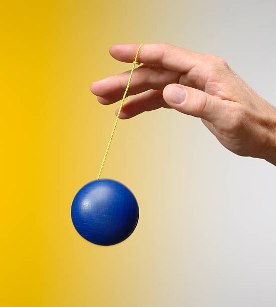 Male hand playing with a blu yo-yo on yellow background stock photo