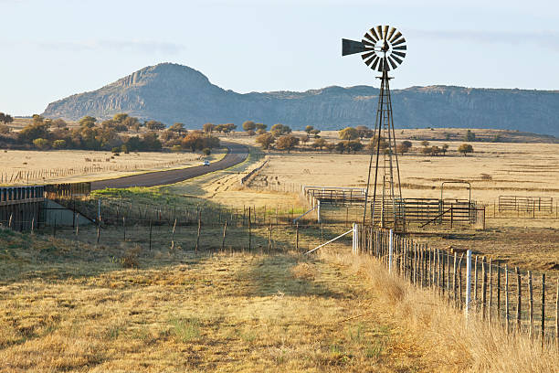 Fence-Line Leading to Ranch Corrals and Windmill "Fence-line leading to West Texas Ranch corrals and windmill, with highway running by. In early morning light." ranch stock pictures, royalty-free photos & images
