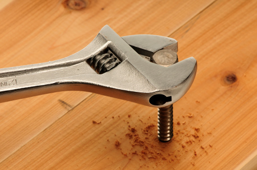 Close-up of an adjustable wrench driving a lag bolt into a board.