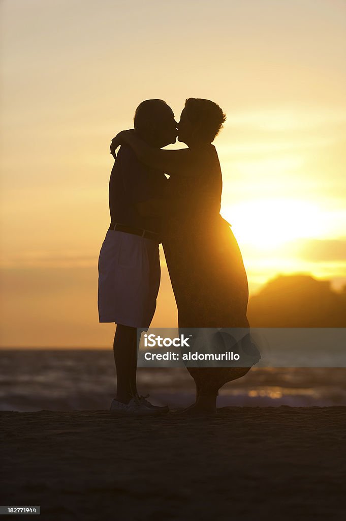 Romantic senior couple kissing Romantic senior couple kissing and enjoying the sunset In Silhouette Stock Photo