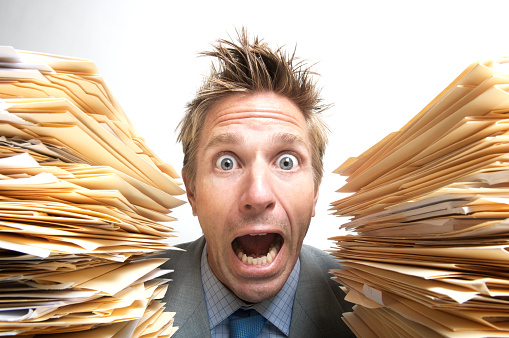 Wide-eyed stressed office worker businessman screaming for help between two massive stacks of file folders white background