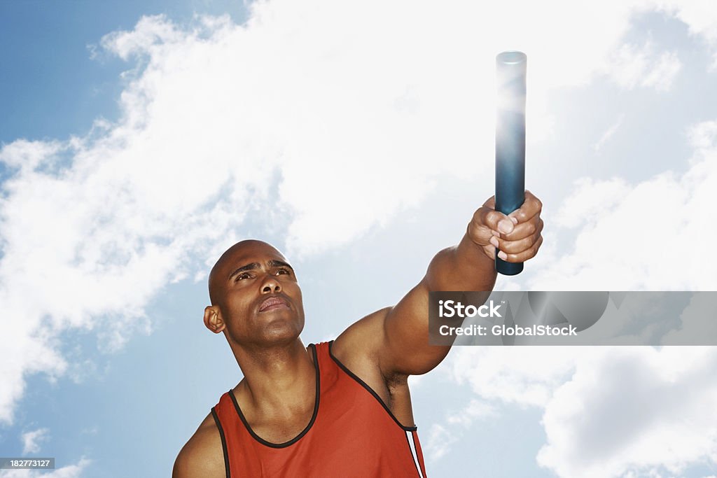 Upward view of an athlete holding a baton against sky Upward view of an African American athlete holding a baton against cloudy sky Relay Stock Photo