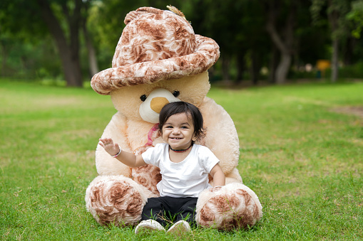 Cute little Boy sitting and playing with huge teddy bear at park or garden.