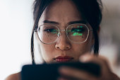 A woman is carefully observing trading charts reflected in her glasses at home