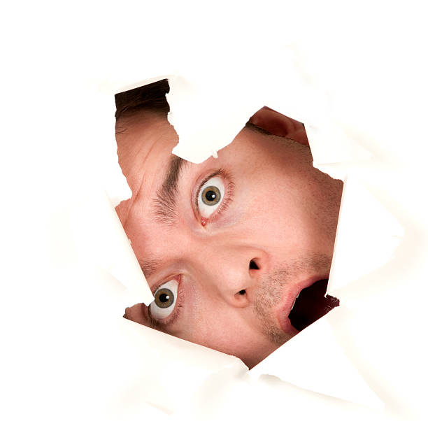 istock Surprised man peeks  through crack in white wall 182774224