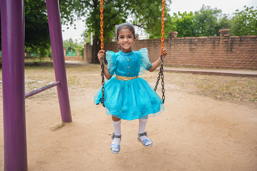 Happy little indian girl having fun on a swing on sunny day. Healthy summer activity for children.