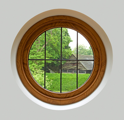 A porthole style window with a garden view in an expensive new home. The mahogany framed leaded glass window has been recessed into a wall. The surrounding finish has been processed to be an even tone to enable easy expansion of canvas size.Looking for a window Please see my window collection including cut-outs with clipping paths by clicking on the Lightbox Link below...