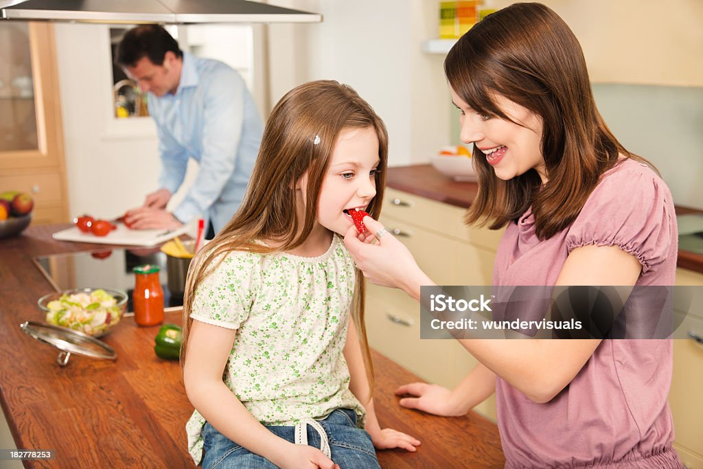 Madre hija de alimentación fresa mientras que hombre Cortando Tomates en - Foto de stock de Adulto libre de derechos