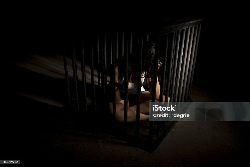 Slavery - Human Trafficking Young woman of mixed ethnicity locked in a cage. Shot in dramatic lighting. Modern day slavery (human trafficking) concept. Human Trafficking Stock Photo