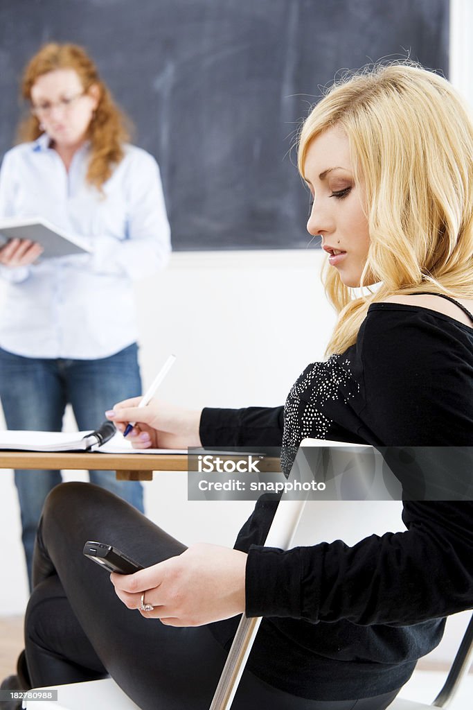 Teen envía un mensaje de texto mientras que en clase - Foto de stock de Salón de clase libre de derechos